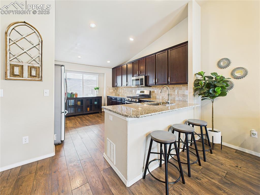 Image 11 of 50: Open layout highlights the breakfast bar seating, warm flooring, and seamle