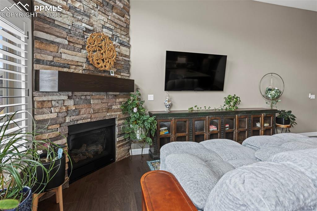 Image 12 of 47: Living area with a stone fireplace, baseboards, and wood finished floors