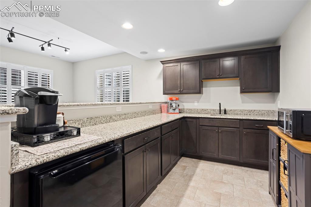 Image 29 of 47: Kitchen with stainless steel microwave, black dishwasher, light stone count