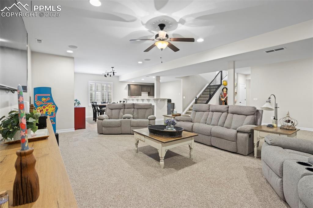 Image 31 of 47: Carpeted living room with visible vents, baseboards, ceiling fan, and stair
