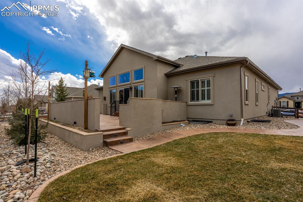 Image 40 of 47: Back of property with a lawn, cooling unit, fence, and stucco siding
