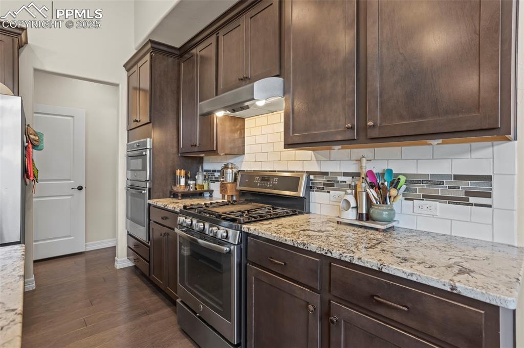 Image 8 of 47: Kitchen featuring dark brown cabinets, backsplash, under cabinet range hood