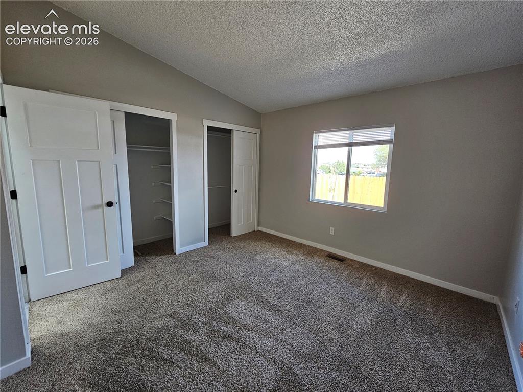 Image 10 of 15: Carpeted room featuring a vaulted ceiling and a window with blinds