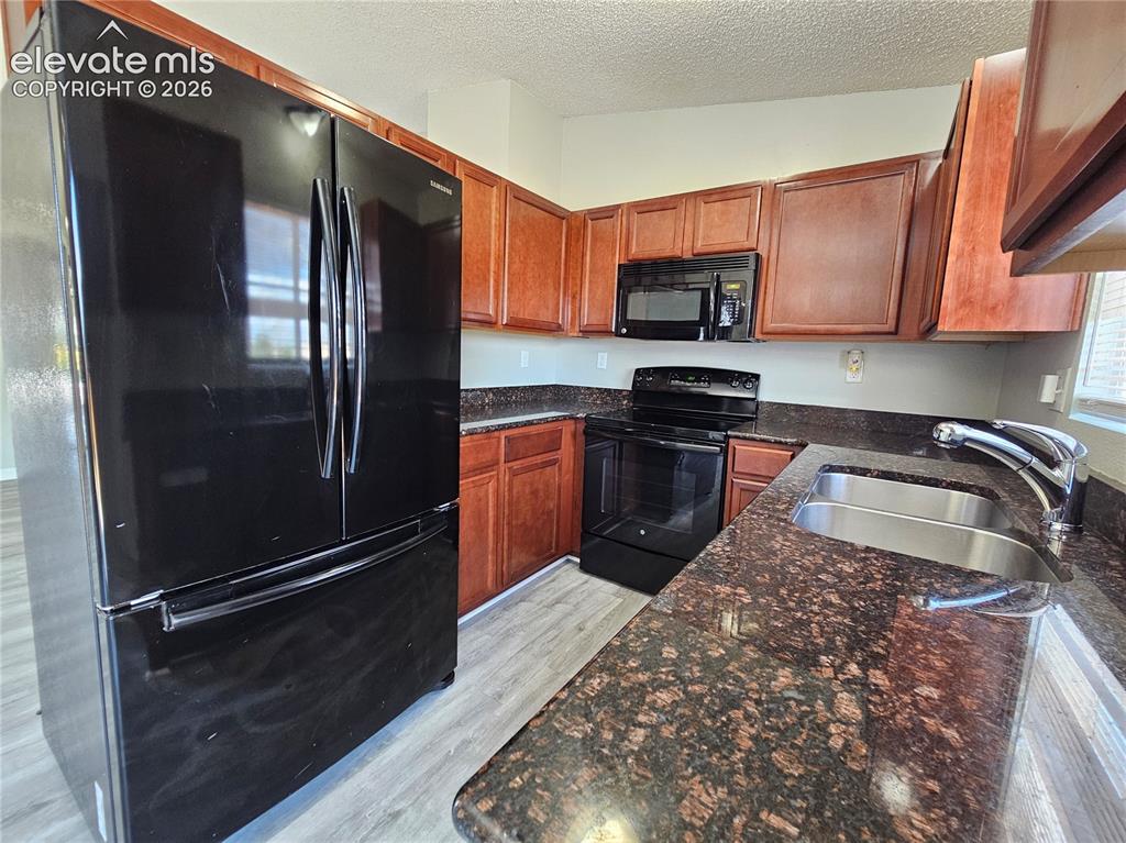 Image 7 of 15: Kitchen featuring wood cabinetry, dark speckled countertops, and wood-finis