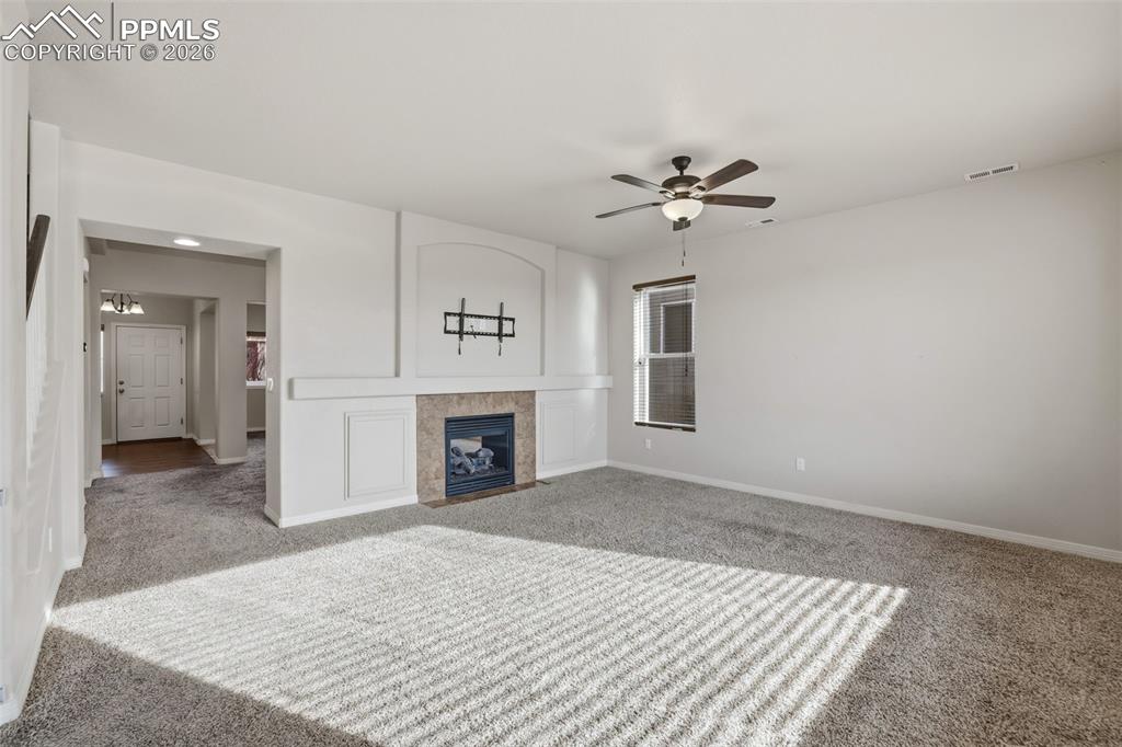 Image 10 of 39: Unfurnished living room with a tiled fireplace, carpet flooring, and a ceil