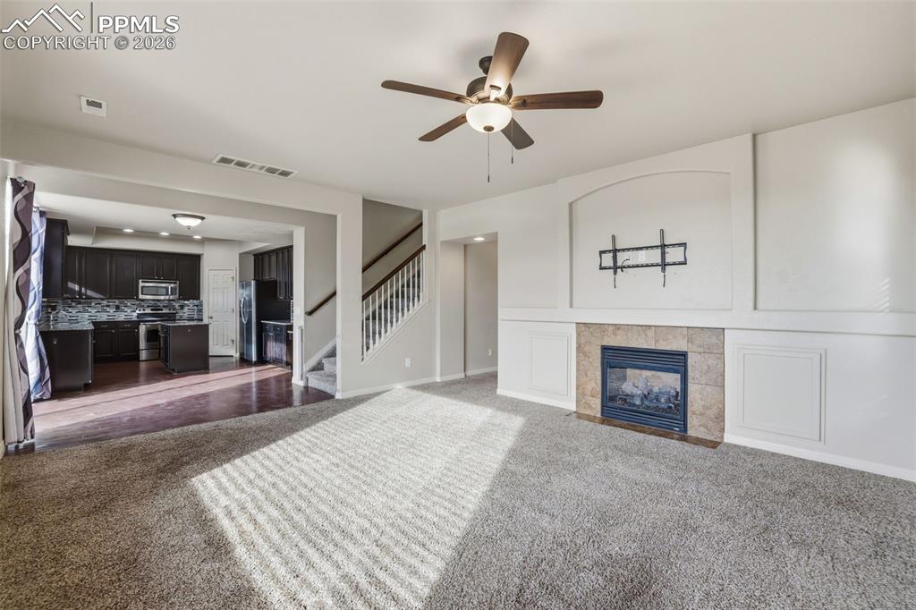 Image 12 of 39: Unfurnished living room with a tile fireplace, carpet flooring, stairway, a