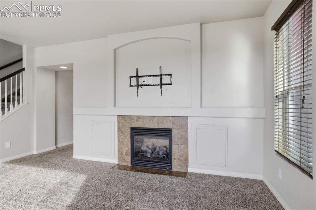 Image 13 of 39: Unfurnished living room featuring a fireplace, carpet, and stairway