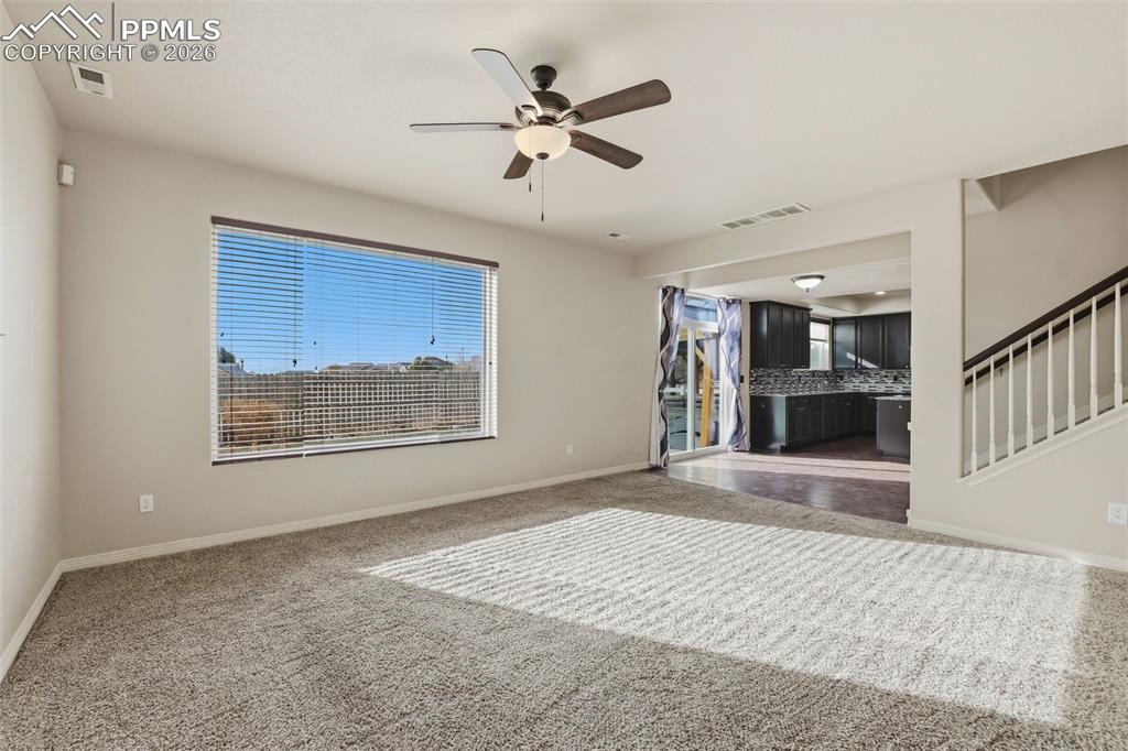 Image 14 of 39: Carpeted empty room with a ceiling fan, plenty of natural light, and stairw