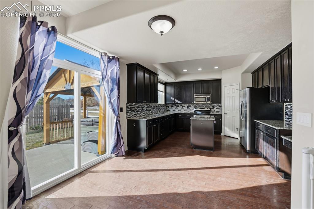 Image 16 of 39: Kitchen with dark cabinets, tasteful backsplash, a center island, stainless