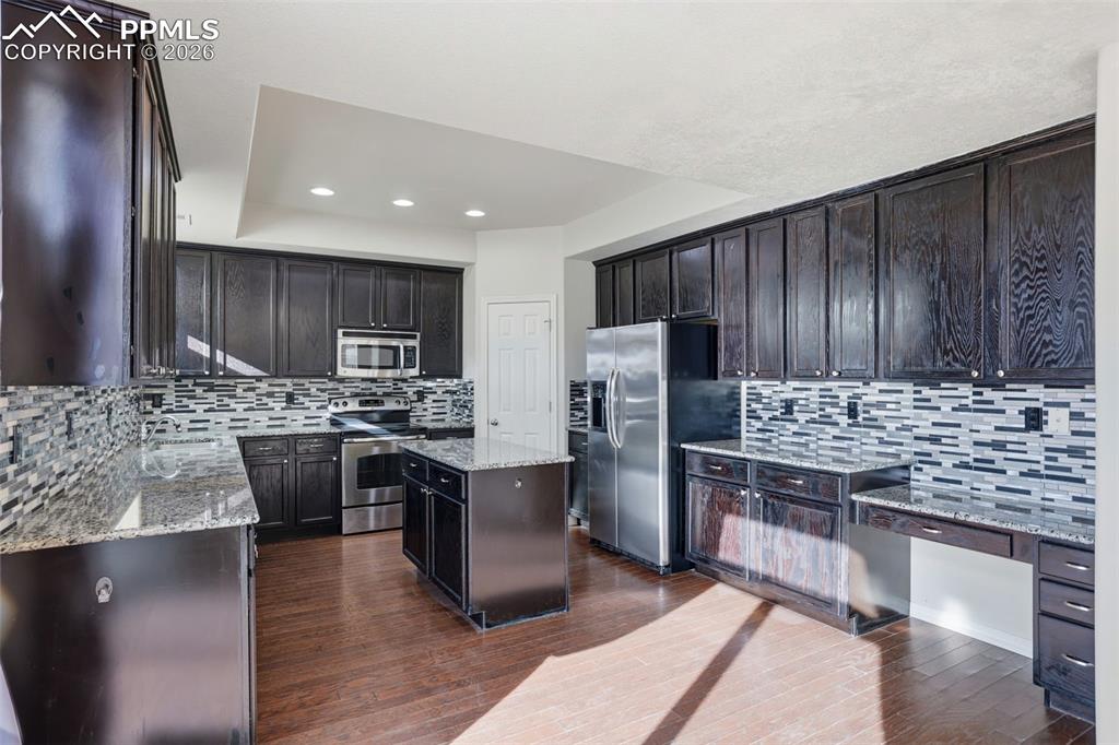 Image 17 of 39: Kitchen featuring light stone counters, stainless steel appliances, a cente