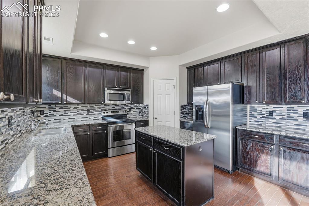 Image 19 of 39: Kitchen featuring stainless steel appliances, a center island, light stone 