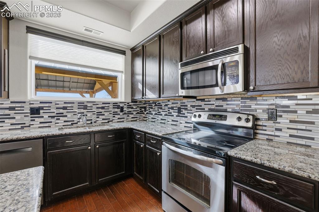 Image 20 of 39: Kitchen featuring appliances with stainless steel finishes, light stone cou