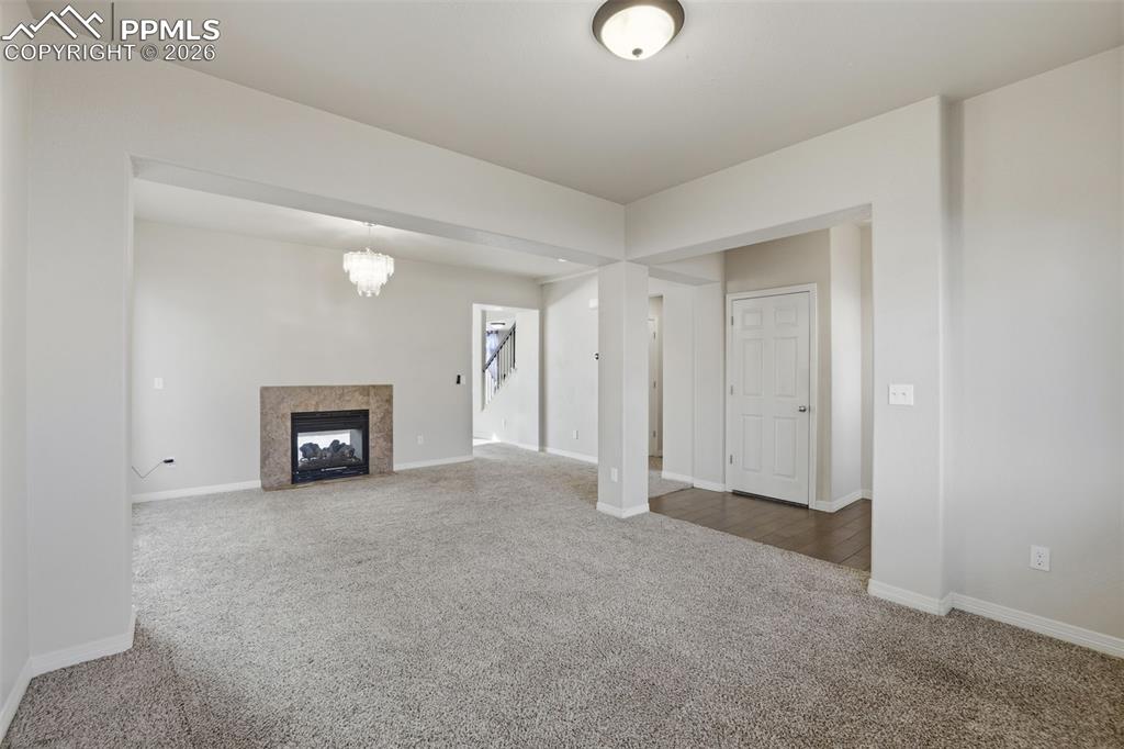 Image 8 of 39: Unfurnished living room with carpet floors, a high end fireplace, and a cha