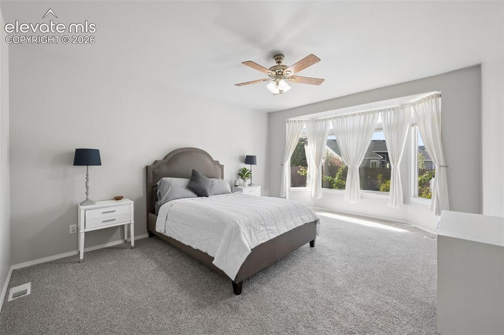 Image 13 of 37: Neutral-toned carpeting, bay window, and a central ceiling fan with integra