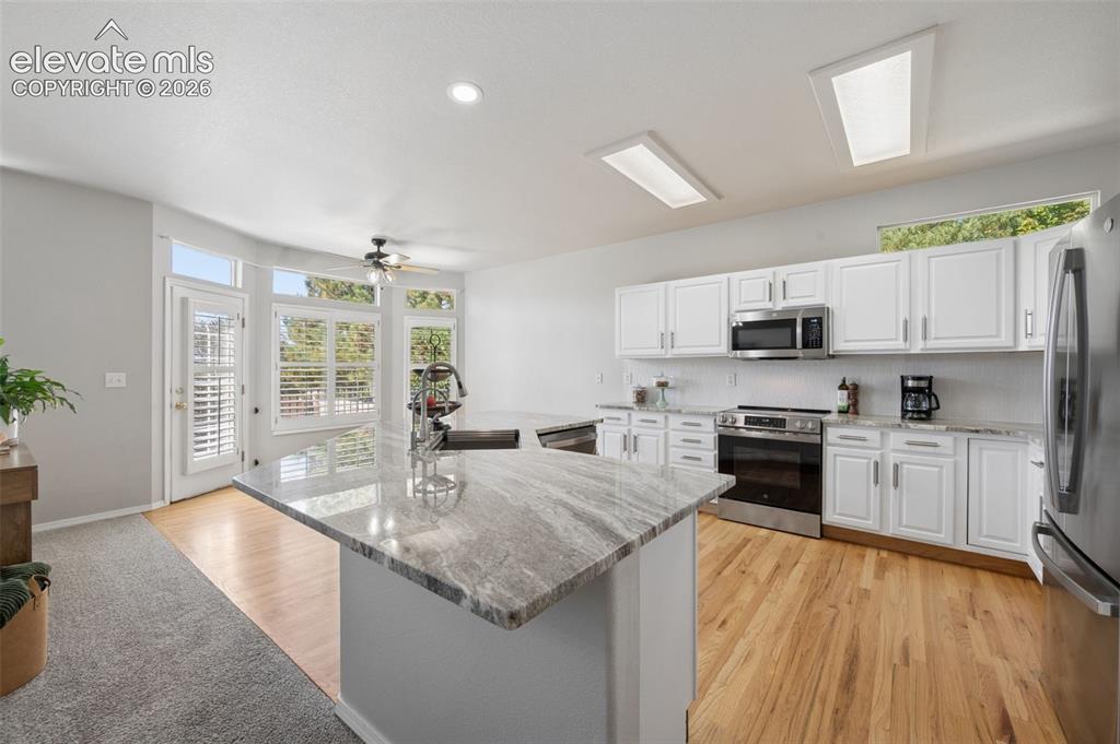 Image 18 of 37: Kitchen featuring stone-topped center island with integrated sink, white ca