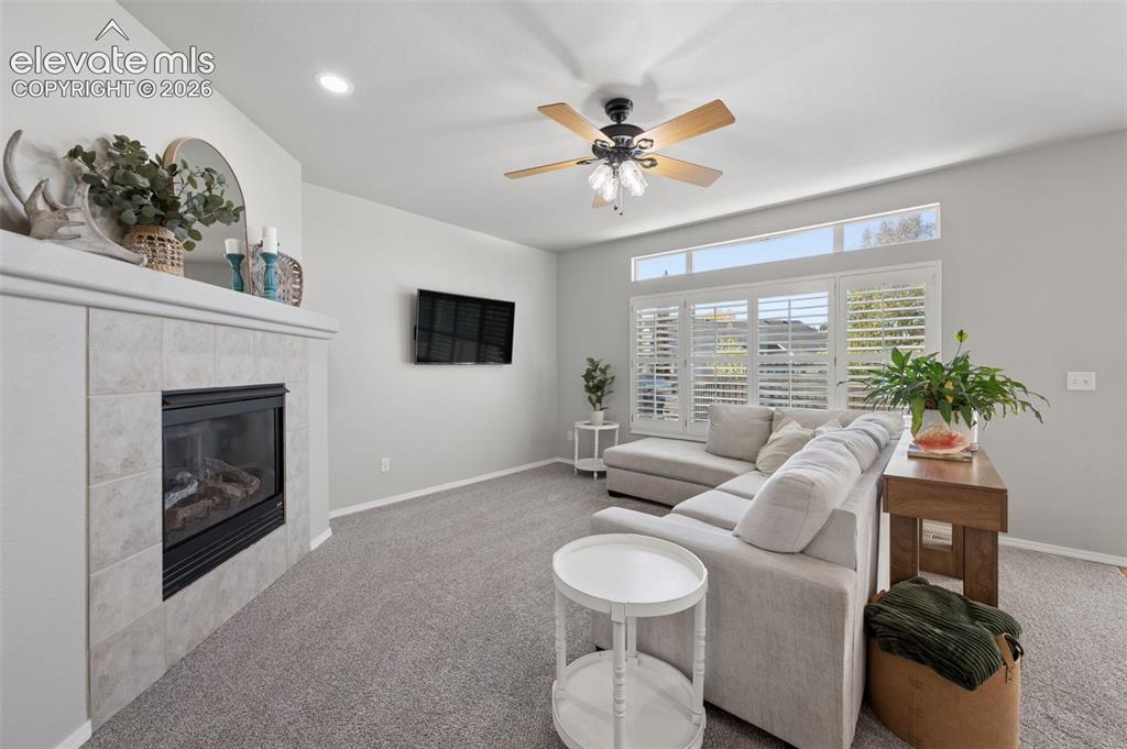 Image 25 of 37: Living area featuring a fireplace with a neutral tile surround, custom tran