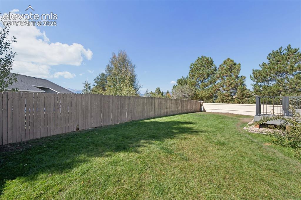 Image 36 of 37: Fenced-in backyard featuring a grass lawn, mature trees, and an elevated co