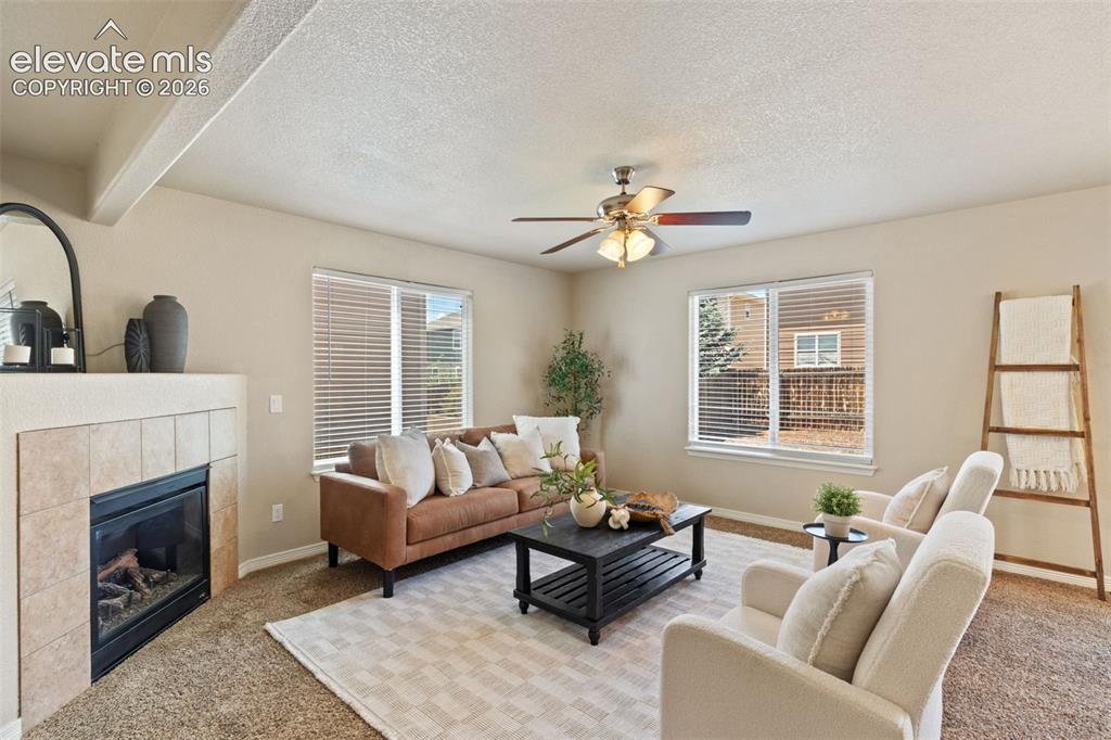 Image 18 of 35: Living area featuring a tiled fireplace, multiple windows with blinds, and