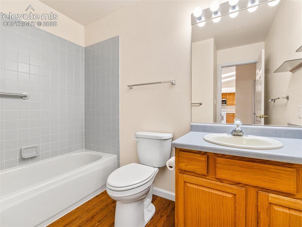 Image 6 of 24: Bathroom featuring a white bathtub, light grey tile surround, wood-finish f