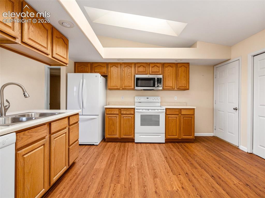Image 8 of 24: Kitchen featuring wood-finish flooring, oak cabinetry, white appliances, an