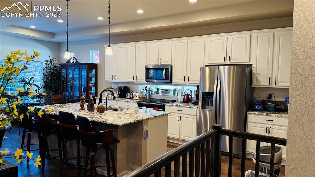 Image 10 of 28: Kitchen with appliances with stainless steel finishes, backsplash, hanging