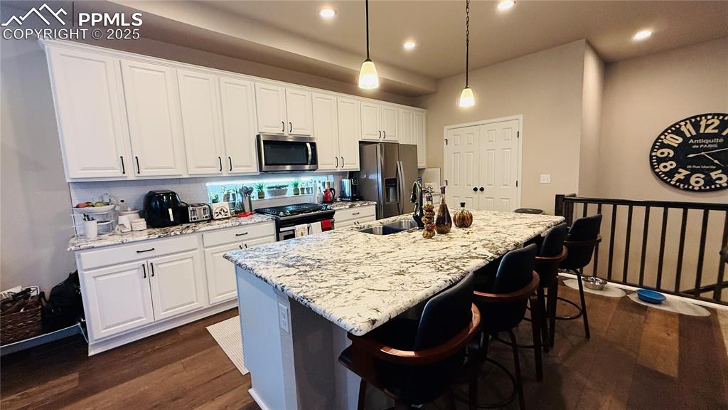 Image 11 of 28: Kitchen with backsplash, dark wood-style floors, a kitchen breakfast bar, w