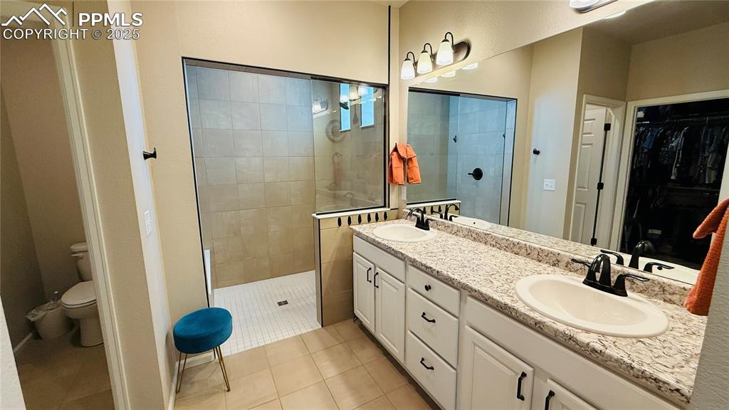 Image 14 of 28: Bathroom featuring a walk in closet, a walk in shower, double vanity, and l