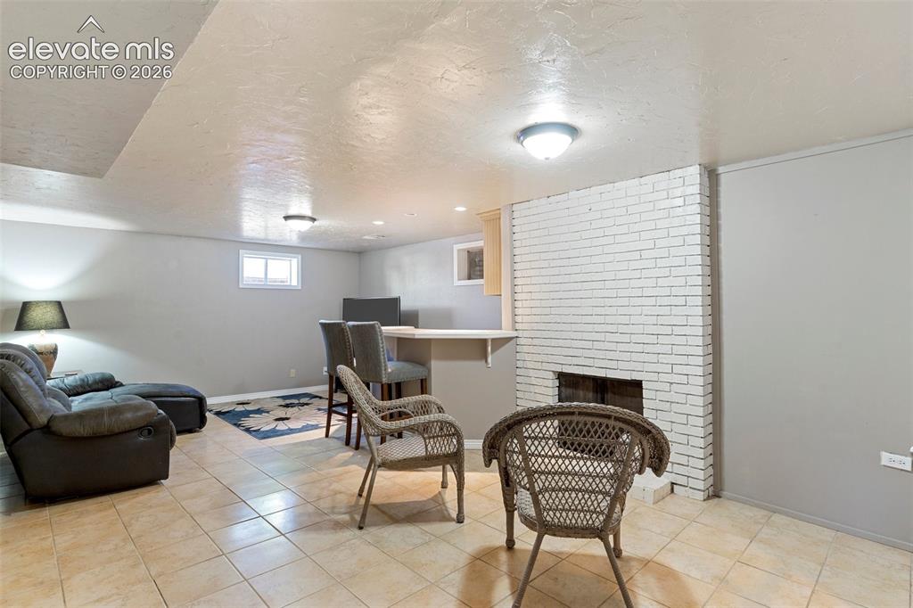 Image 16 of 24: Living room featuring a textured ceiling, brick wall, a brick fireplace, an