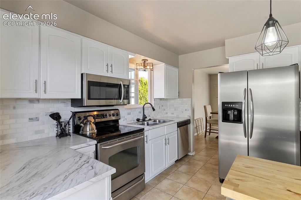 Image 7 of 24: Kitchen with white cabinetry, sink, backsplash, and stainless steel applian