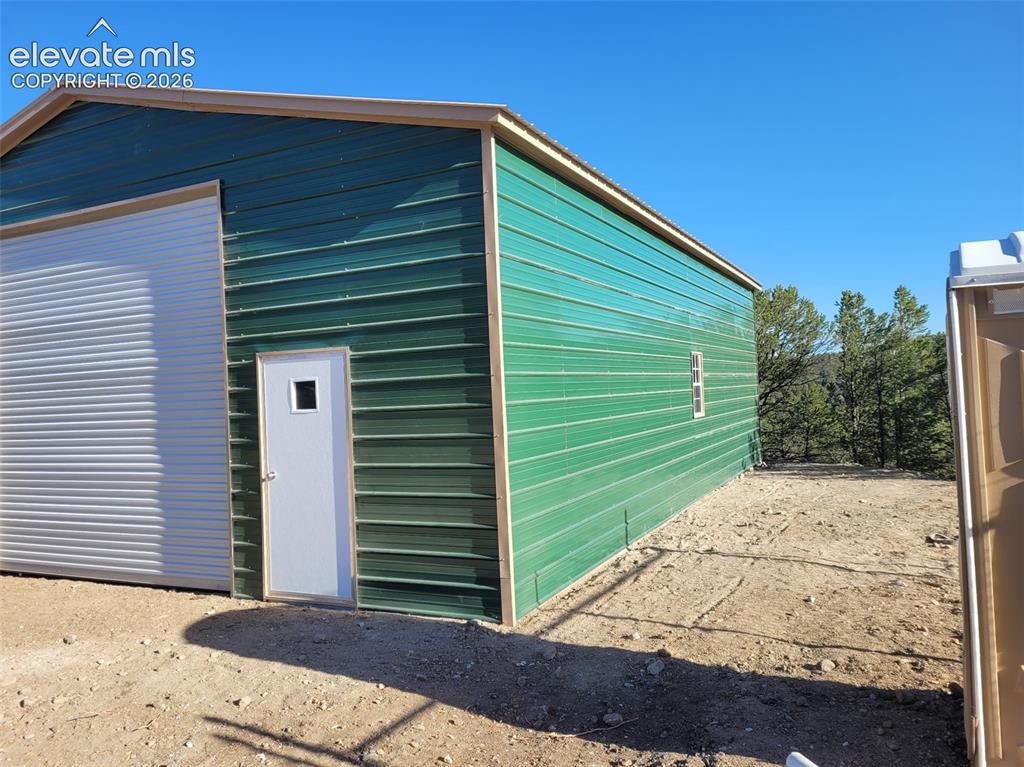 Image 21 of 33: Metal building with a green exterior, featuring a roll-up garage door, an e