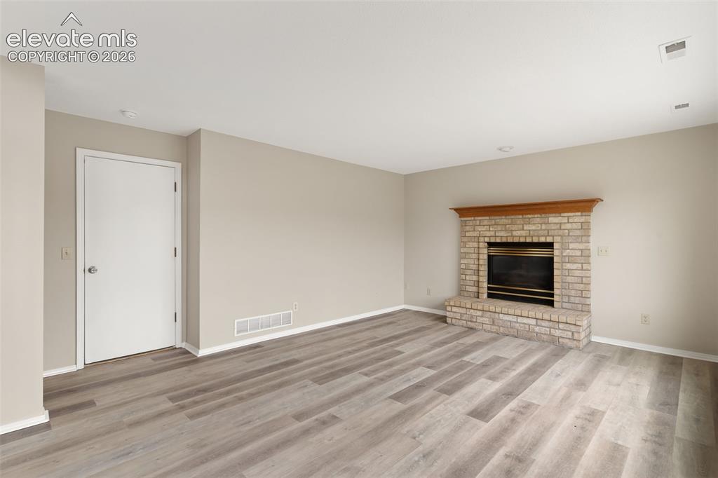 Image 17 of 38: Spacious room featuring light wood-finish flooring, a brick fireplace with 
