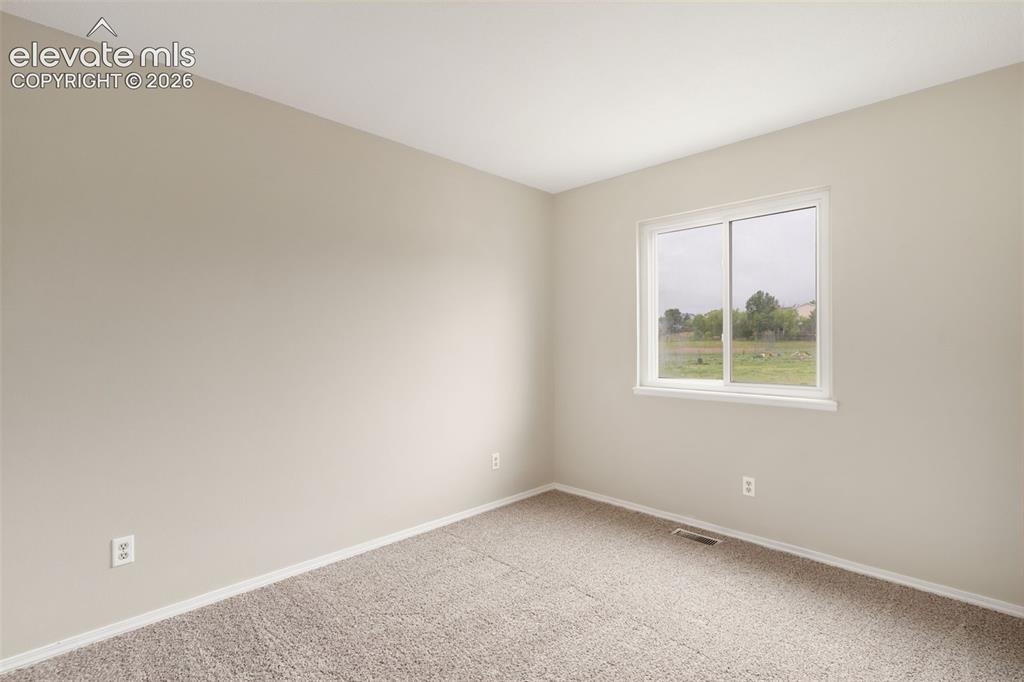 Image 26 of 38: Neutral-toned room with plush carpeting, a single window featuring a white 
