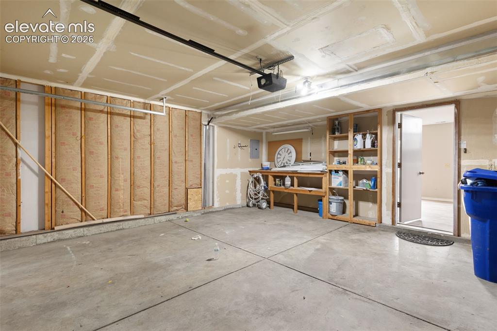 Image 36 of 38: Spacious garage featuring a concrete floor, built-in wooden shelving, a wor