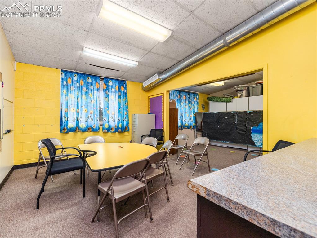 Image 34 of 49: Carpeted dining room featuring a paneled ceiling and concrete block wall