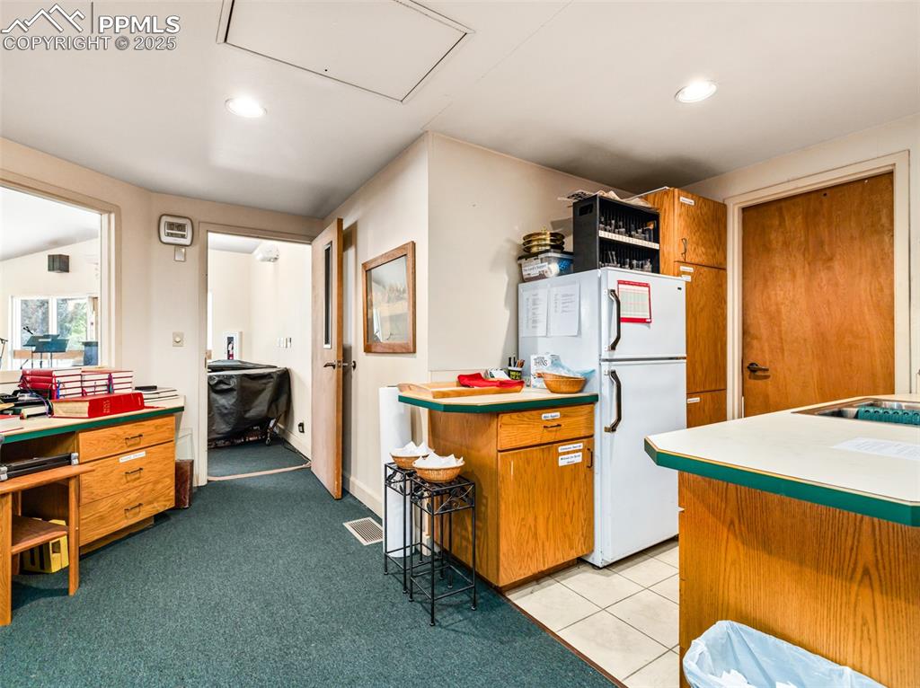 Image 45 of 49: Kitchen featuring brown cabinets, freestanding refrigerator, light countert