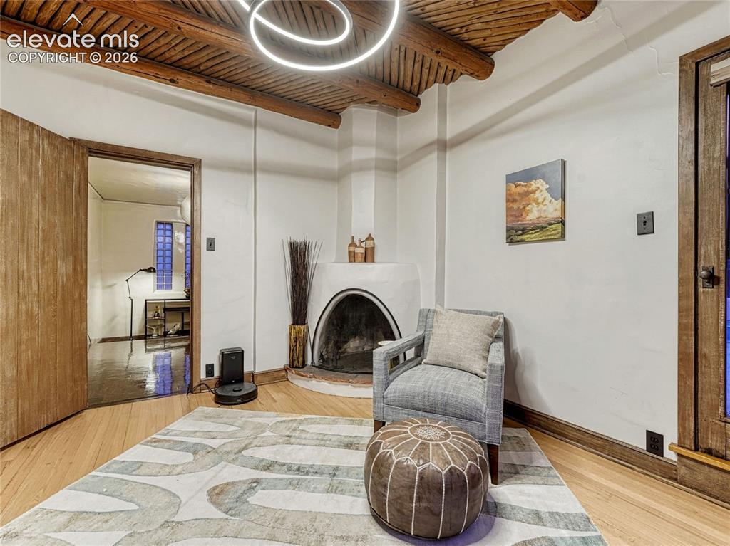 Image 20 of 50: Primary Suite sitting room w/Kiva fireplace & Vigas ceiling.
