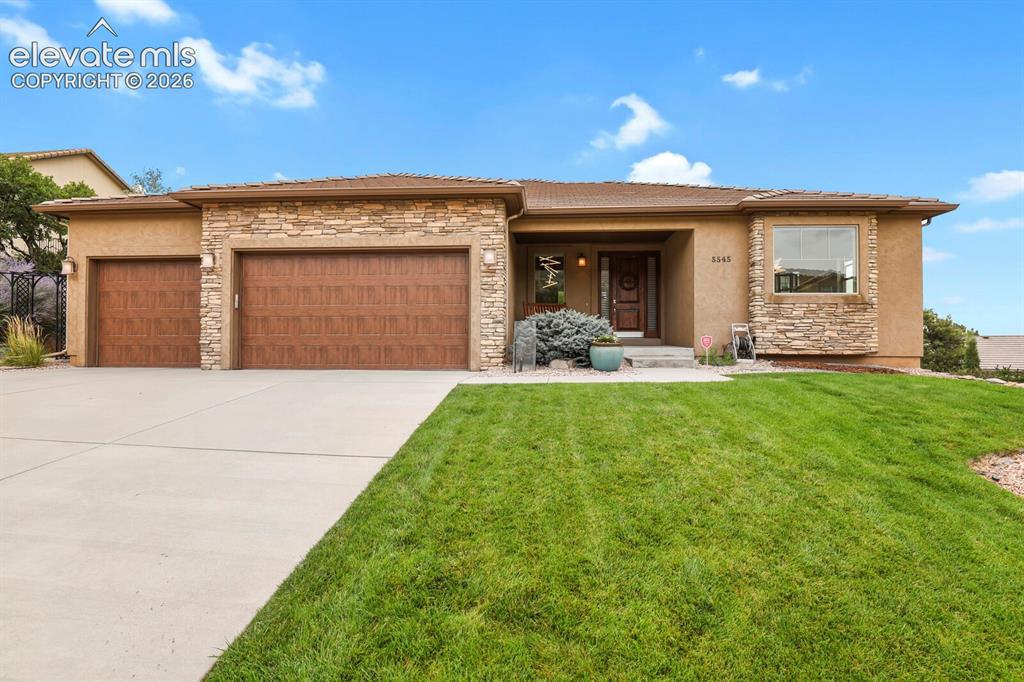 Image 2 of 48: Stucco exterior with stone accents, wood-finish garage doors, concrete driv