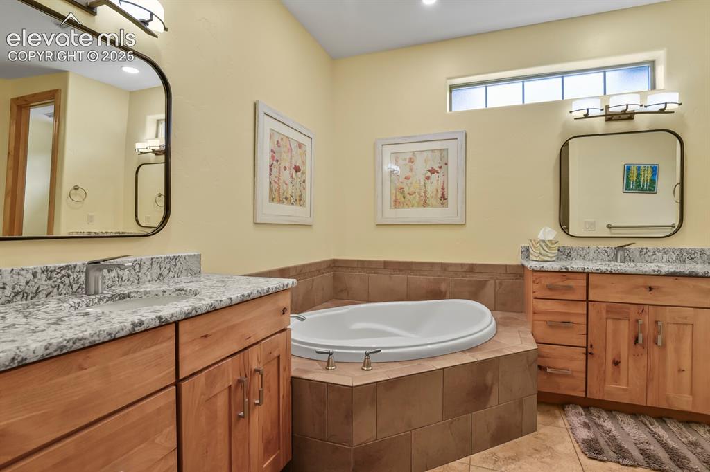 Image 20 of 48: Dual wood-finish vanities with stone countertops, a built-in soaking tub wi