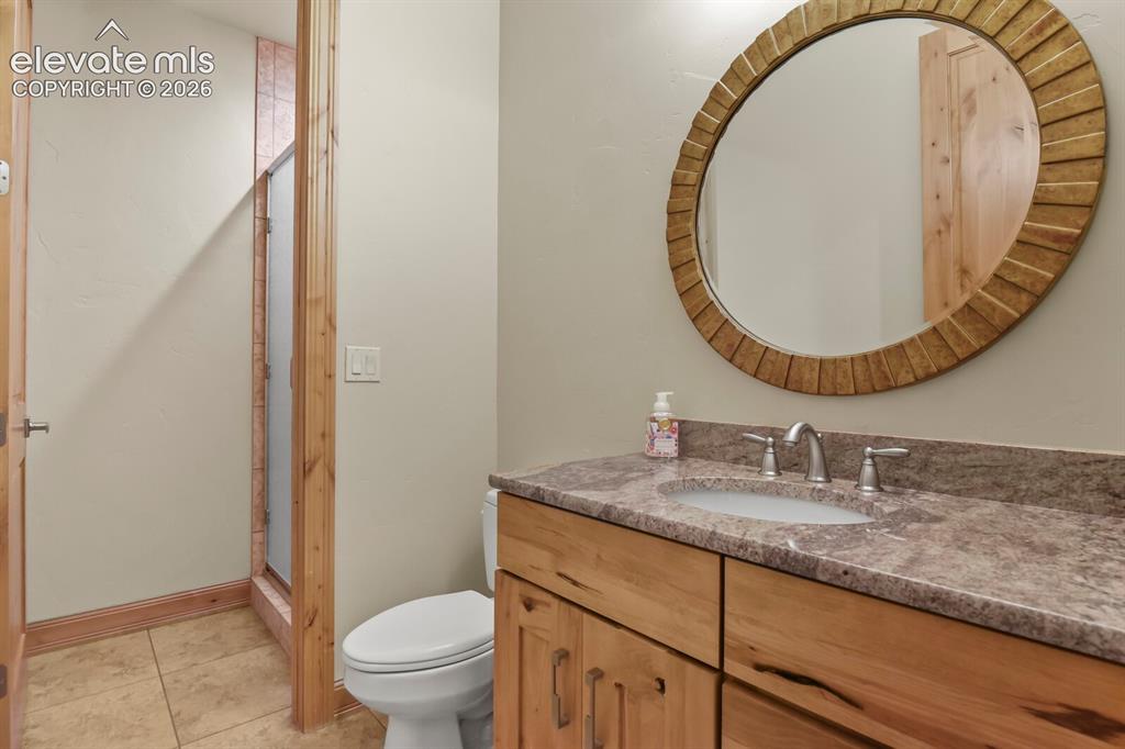 Image 24 of 48: Main level bathroom featuring a wood-finish vanity cabinetry with stone cou