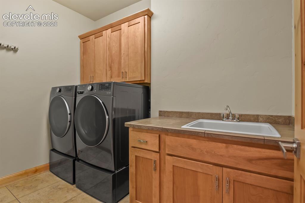 Image 25 of 48: Laundry area featuring wood-finish cabinetry, a utility sink with a stainle