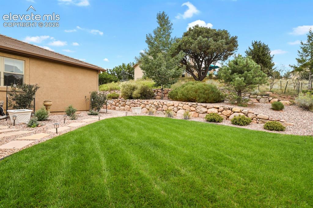Image 38 of 48: Lawn area with a stone paver pathway, terraced landscaping featuring natura