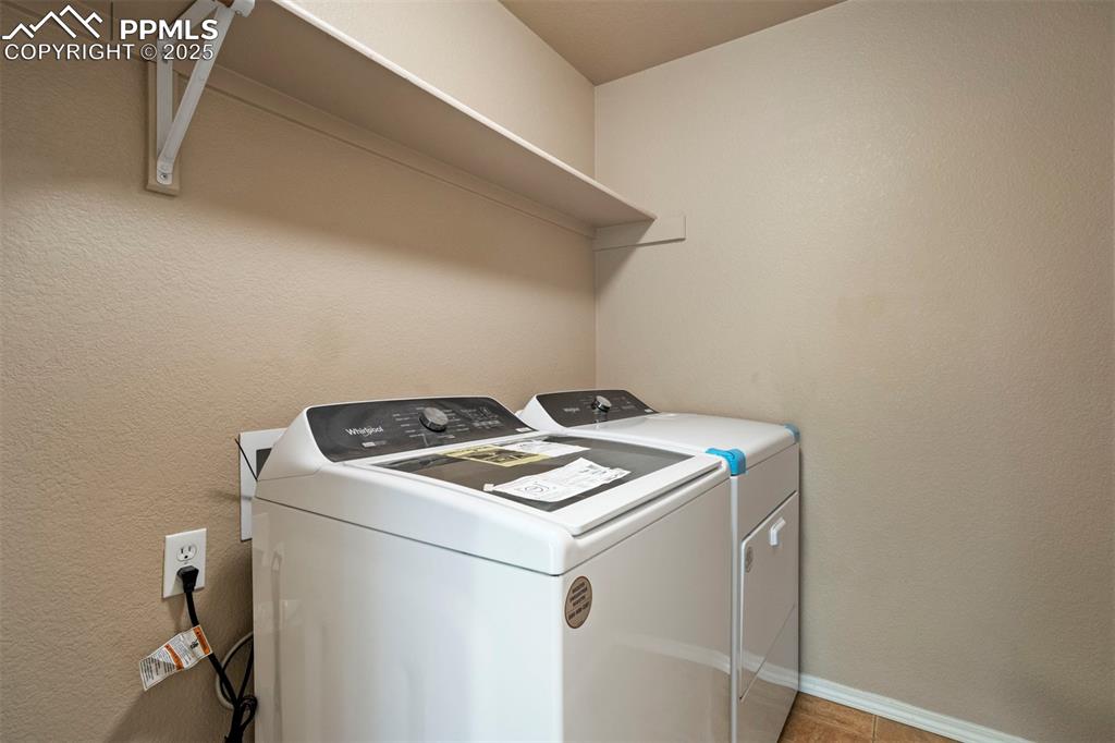 Image 21 of 50: Laundry room with a textured wall, washing machine and dryer, and light til