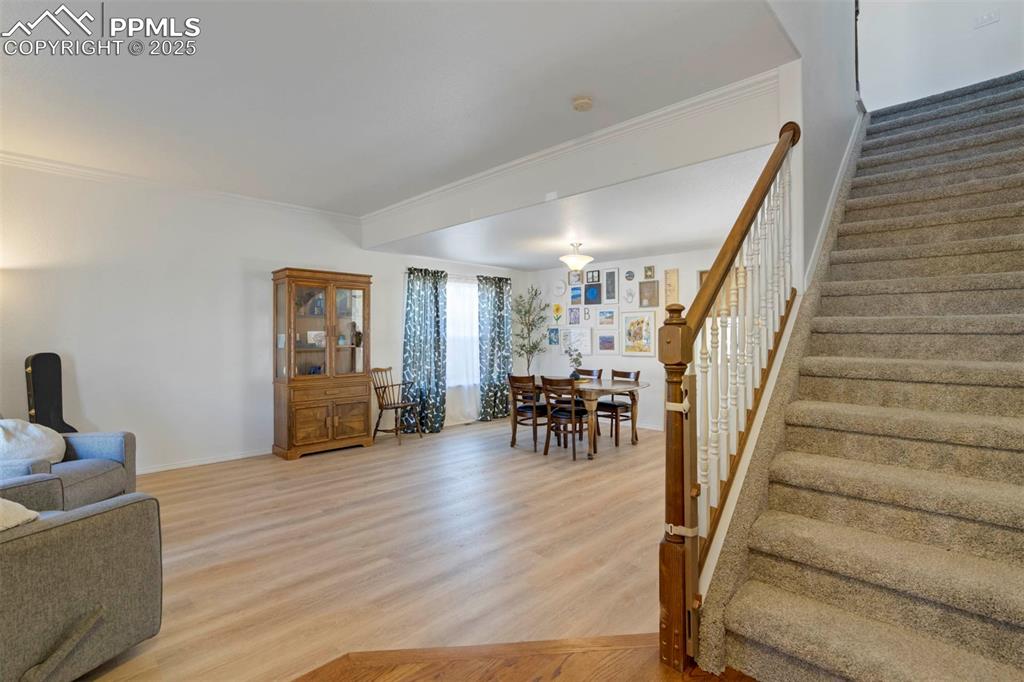 Image 22 of 50: Living area with light wood-style flooring, stairs, and ornamental molding