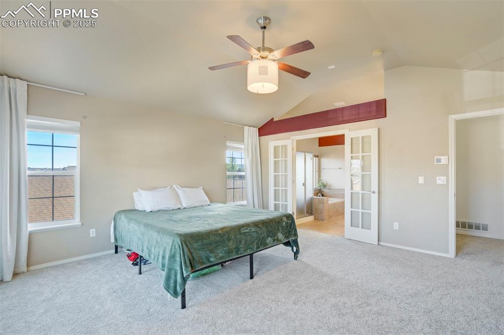 Image 25 of 50: Bedroom with french doors, light carpet, lofted ceiling, and a ceiling fan