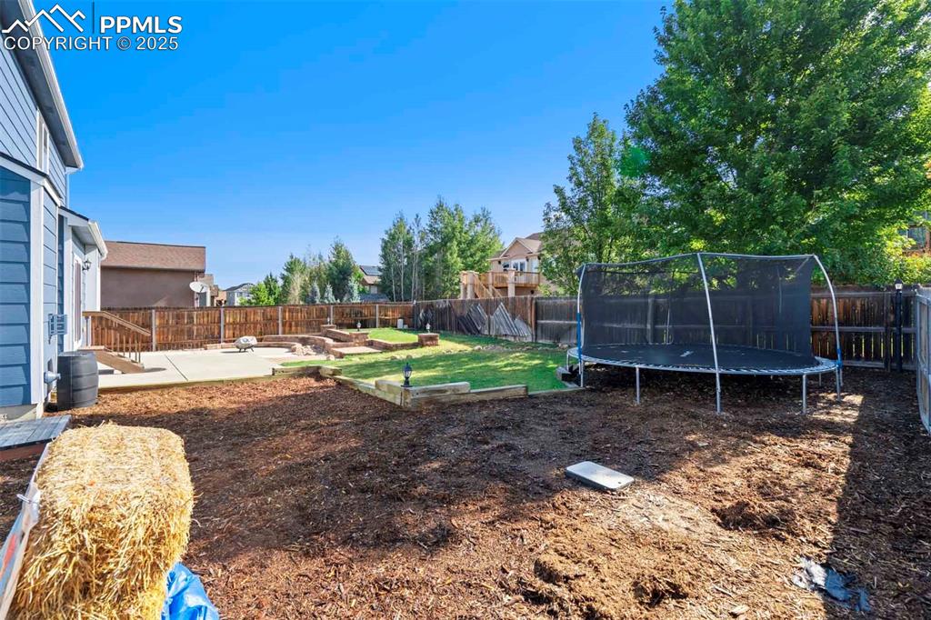 Image 46 of 50: Fenced backyard with a patio area, a trampoline, and a vegetable garden