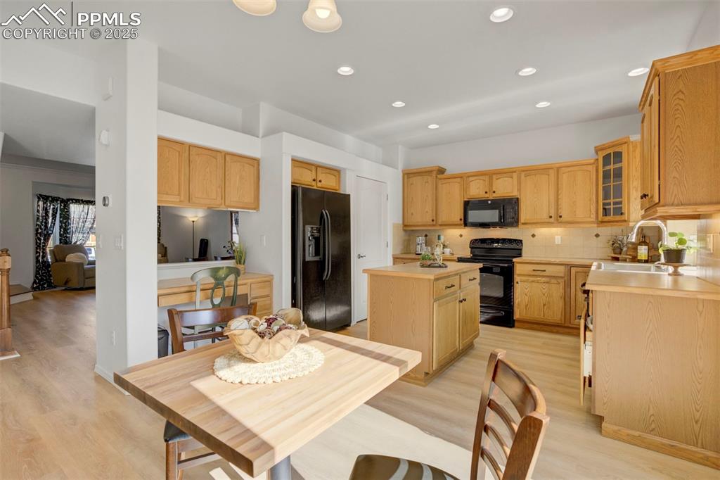 Image 9 of 50: Kitchen with light countertops, tasteful backsplash, black appliances, ligh