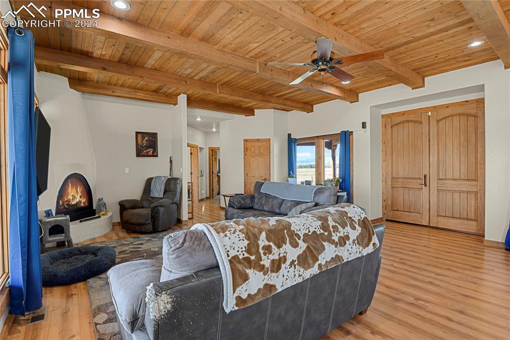 Image 28 of 45: Living room featuring beam ceiling, ceiling fan, a large fireplace, wood ce