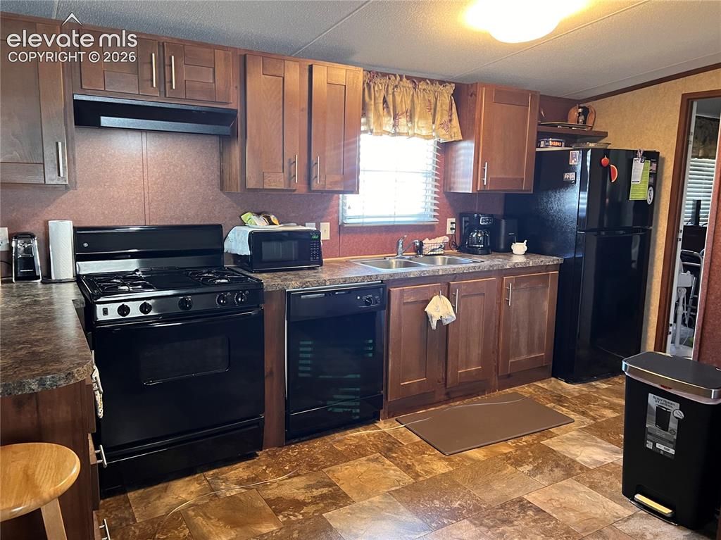 Image 4 of 16: Kitchen with wood-finish cabinetry, dark countertops, and patterned vinyl f