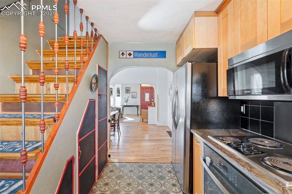 Image 16 of 37: Kitchen featuring arched walkways, dark countertops, black appliances, ligh