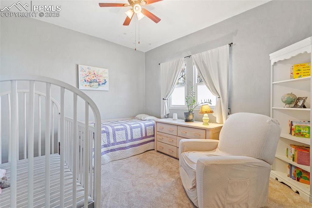 Image 17 of 37: Bedroom with light carpet, a nursery area, and a ceiling fan
